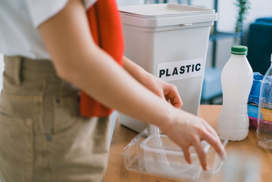 In the foreground, a person wearing beige trousers and a white shirt with an orange sleeve is seen placing a clear plastic container, possibly a food or storage container, on a wooden surface. Behind